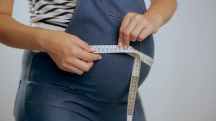 Pregnant woman measuring her belly while standing against a white background. - Powered by Adobe