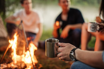 close up cropped photo. focus on the man's hand holding metal cup. hikers on the blurred background...