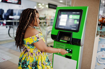 Cute small height african american girl with dreadlocks, wear at coloured yellow dress, against ATM...
