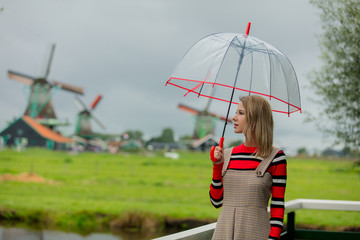 Young girl in dress with umbrella stay on bridge with dutch mills on background. Netherlands