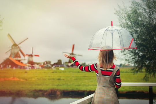 Young girl in dress with umbrella stay on bridge with dutch mills on background. Netherlands