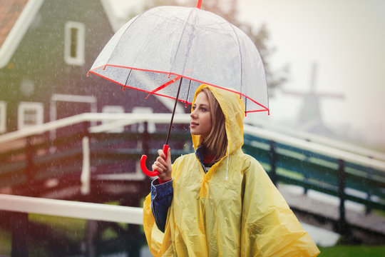 Young girl in rain suit with umbrella stay on bridge with dutch mills on background. Netherlands