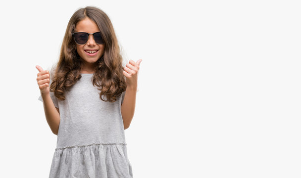 Brunette hispanic girl wearing sunglasses success sign doing positive gesture with hand, thumbs up smiling and happy. Looking at the camera with cheerful expression, winner gesture.