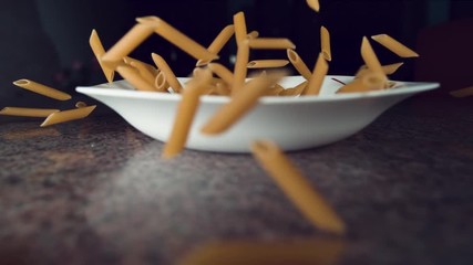 REVERSED SUPER SLOW MOTION, CLOSE UP, DOF: Uncooked yellow macaroni bouncing into the white plate and back into the air. Cool shot of food getting rebounding of the colorful marble kitchen countertop. - Powered by Adobe