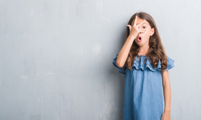 Young hispanic kid over grunge grey wall peeking in shock covering face and eyes with hand, looking through fingers with embarrassed expression.
