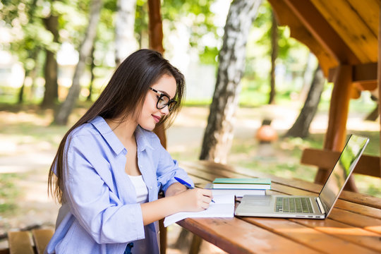 Portrait foreign or foreigner student. Attractive woman is using pen for writing note on notebook while open laptop. Charming beautiful girl is university student.