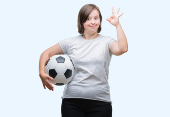 Young adult woman with down syndrome holding soccer football ball over isolated background doing ok sign with fingers, excellent symbol