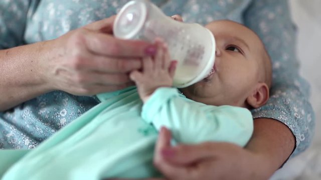 Grandmother feeds grandson from a bottle. Little baby boy on the hands of grandma. Three-month-old baby boy drinks milk, artificial feeding