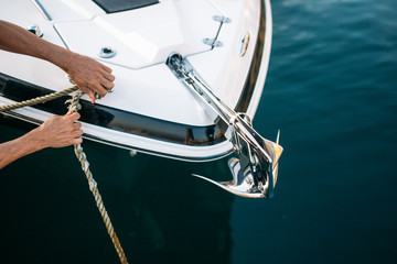 Man s hand with boat rope. Yachtsman moors his motor boat at jetty. Close up hands and bow of the...