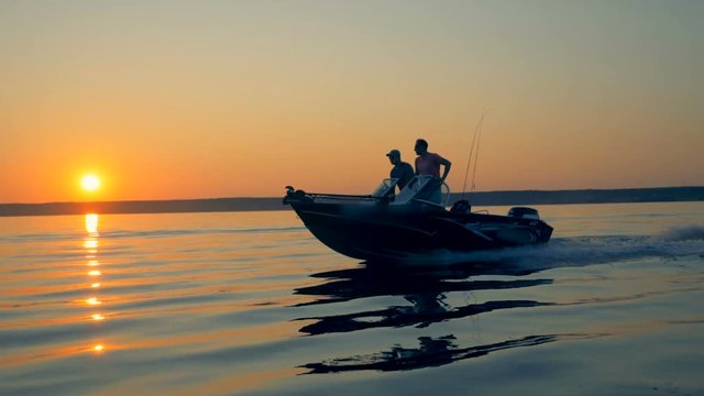 Sunrise scenery with two anglers driving a motorboat. Friendship, best friends concept.