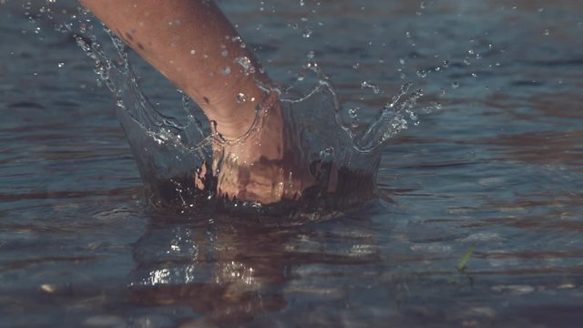 SLOW MOTION, CLOSE UP, DOF: Unrecognizable violent person punching the surface of a glassy lake in the wilderness. Angry human relieving stress by striking the river and splashing the clear water.
