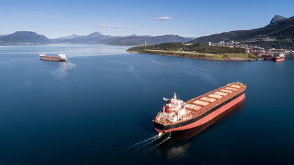 Aerial shot of a cargo ship on the open sea with other ship and mountains in the background,...