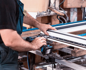 Production windows pvc, man screwed screwdriver hinged defense on the sash pvc frame, close-up, work