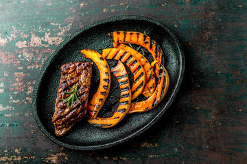Grilled meat and pumpkin on black plate. Autumn menu. Top view