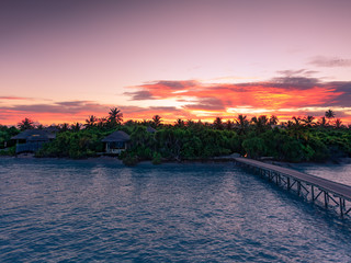 Sunset at Olhuveli Island Maldive with red fiery sky and lagoon ocean water with pier