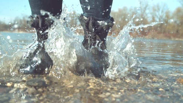 SLOW MOTION, CLOSE UP Cheerful girl stomping her feet in the shallow lake and splashing glassy water around her. Playful woman jumping around the calm river. Unrecognizable female enjoying in the fall