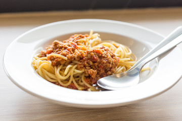 Cuisine and Food, Italian spaghetti pasta with meat and tomato sauce in a white plate on a wooden table.