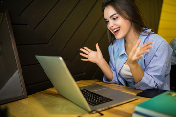 Shocked woman holding laptop screen looking surprised in coffee shop