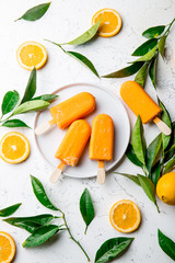Homemade orange ice cream on stick. white background with orange fruits slices and orange tree leaves. Orange popsicles lollipop