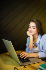 Young student woman with laptopin gray dress sitting at table in cafe. Freelancer working in coffee shop. Student learning online.