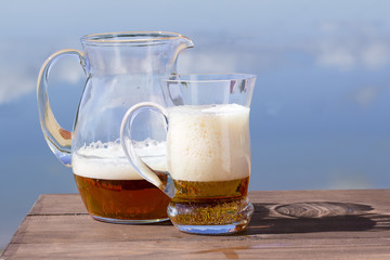 Pitcher with a mug of fresh beer on the table by the lake