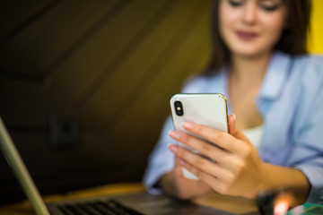 Young woman with laptop typing on phone while sitting in cafe