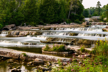 Long Exposure Of Sauble Falls With Soft Water Flowing Over The Rocks With Trees And Bushes In The Background
