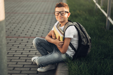 Obraz premium Portrait of a Little Boy in White T-Shirt and Jeans Holding Books in Hands Outdoors