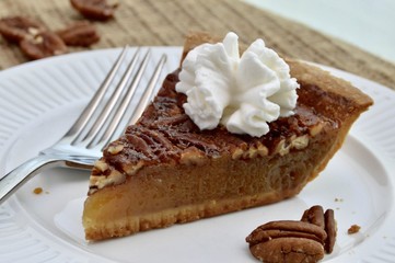 Slice of pecan pie with whipped cream on a white plate