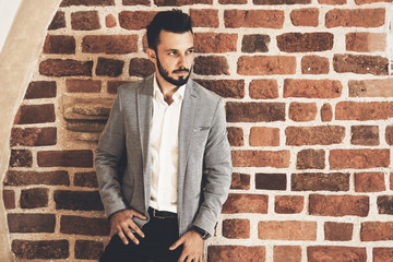 Elegant fashionable man in a jacket posing on the background of an old archival brick wall