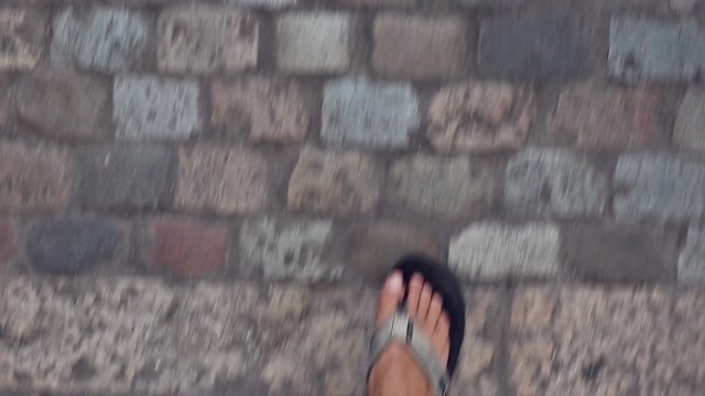 Man feet walking on sandals on a cobble stone street