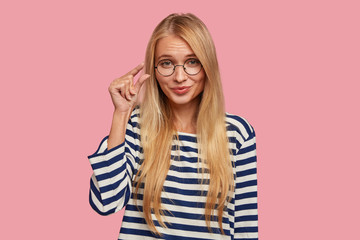 Blonde woman gestures indoor, shows something very tiny with hand, needs how much attention she...