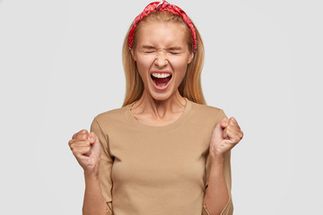 Photo of desperate blonde woman clenches fists, keeps mouth wide opened, expresses negativity,...