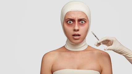Indignant displeased female patient recieves hypodermic anesthesia vaccination before operation, going to have skin resurfacing, has bruises and inflamed epidermis, isolated over white background