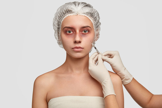 Medicine and reconstructive treatments concept. Wounded patient with bruises, debrides dead tissue, being injected by surgeon in face, prepares for skin grafting, wears medical cap, isolated on white