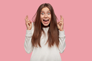 Photo of glad emotive teenager keeps index fingers crossed, believes in something wonderful, stares...