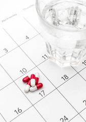 Pills with glass of water on the calendar.