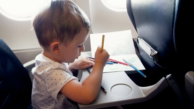 4k footage of little smiling boy drawing on passenger seat at aircraft during flight