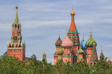 Fototapeta na wymiar Domes of St. Basil's Cathedral on Red square with Spasskaya tower of Moscow Kremlin against green trees and cloudy sky at summer day