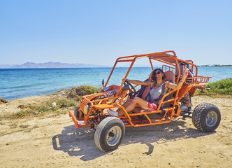 A happy girl driving a Buggy on a dune of beach with the Aegean sea in background. Greek island of...