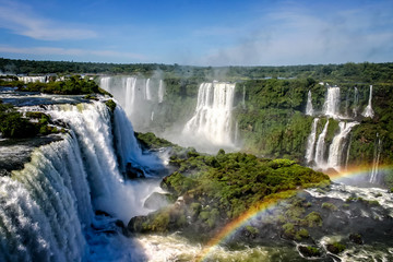 Water cascading over the Iguacu falls with rainbow in foreground in Brazil - obrazy, fototapety, plakaty