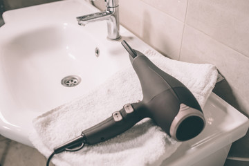 Hair dryer is lying on sink in bathroom. There is white towel undereneath it. Device is prepared to...
