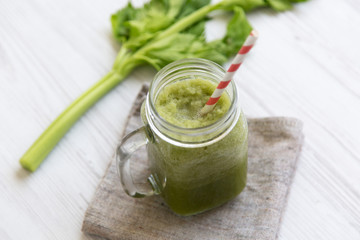 Glass jar of green celery smoothie on white wooden background, low angle view. Close-up.