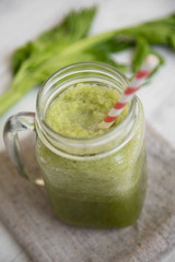 Glass jar of green celery smoothie on white wooden background, low angle view. Close-up.