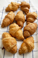 Fresh croissants on cloth on white wooden background, high angle view. Closeup.
