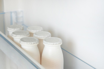 White bottles of dairy product on shelf of open empty refrigerator. Weight loss diet concept.