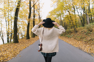 Hippie girl with old camera in a knitted sweater and hat walks autumn park.