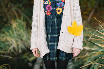 Hippie girl with a yellow maple leaf in a knitted sweater and hat walks autumn park.
