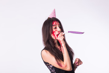 Halloween and carnival concept - young woman with blood on face celebrate holidays with whistle