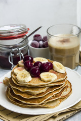 Pancakes with banana and cherries on the top and a cup of coffee